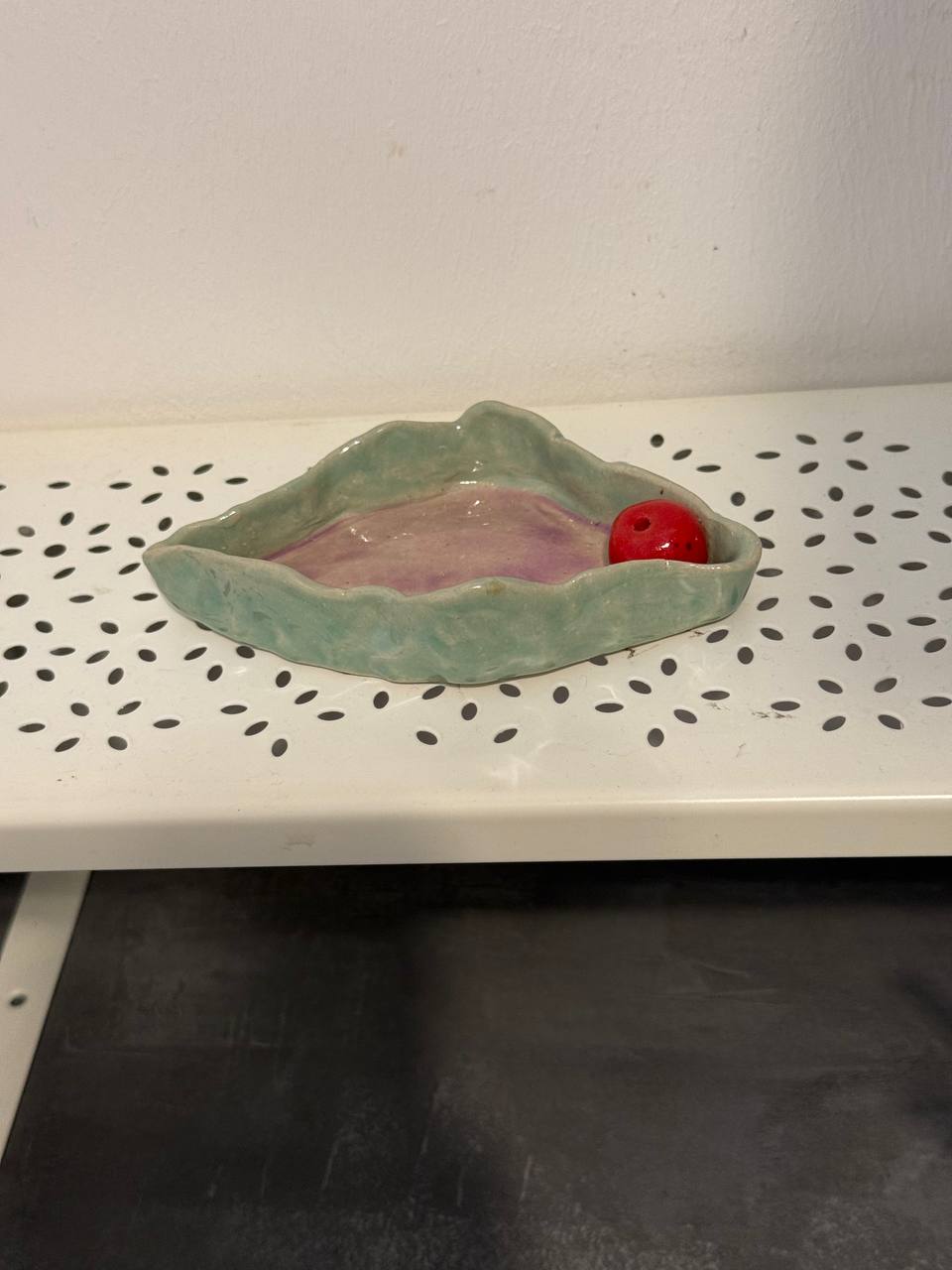 Flache Schale mit welligem Rand, außen mintgrün, innen rosa-lila glasiert, darin eine rote Kugel